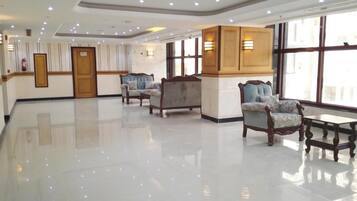 Un vestíbulo de hotel con piso pulido, zona de estar con sillones, un mostrador de recepción y grandes ventanales que permiten la entrada de luz natural.