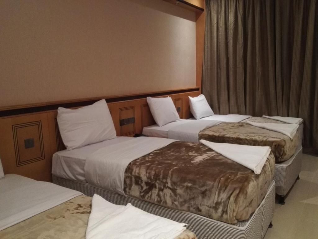 Habitación de hotel con tres camas, un cabecero de madera y un ventanal con cortinas.