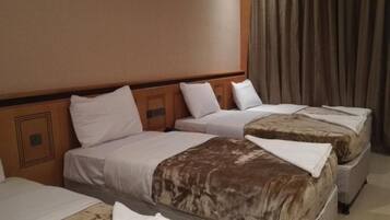 Habitación de hotel con tres camas, un cabecero de madera y un ventanal con cortinas.