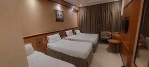 Habitació d'hotel amb tres llits, una zona de seients petita, una televisió i un quadre al mur.