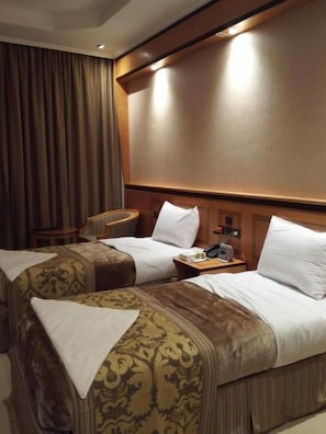 Habitación de hotel con dos camas, una mesita de noche, una silla y un ventanal con cortinas.
