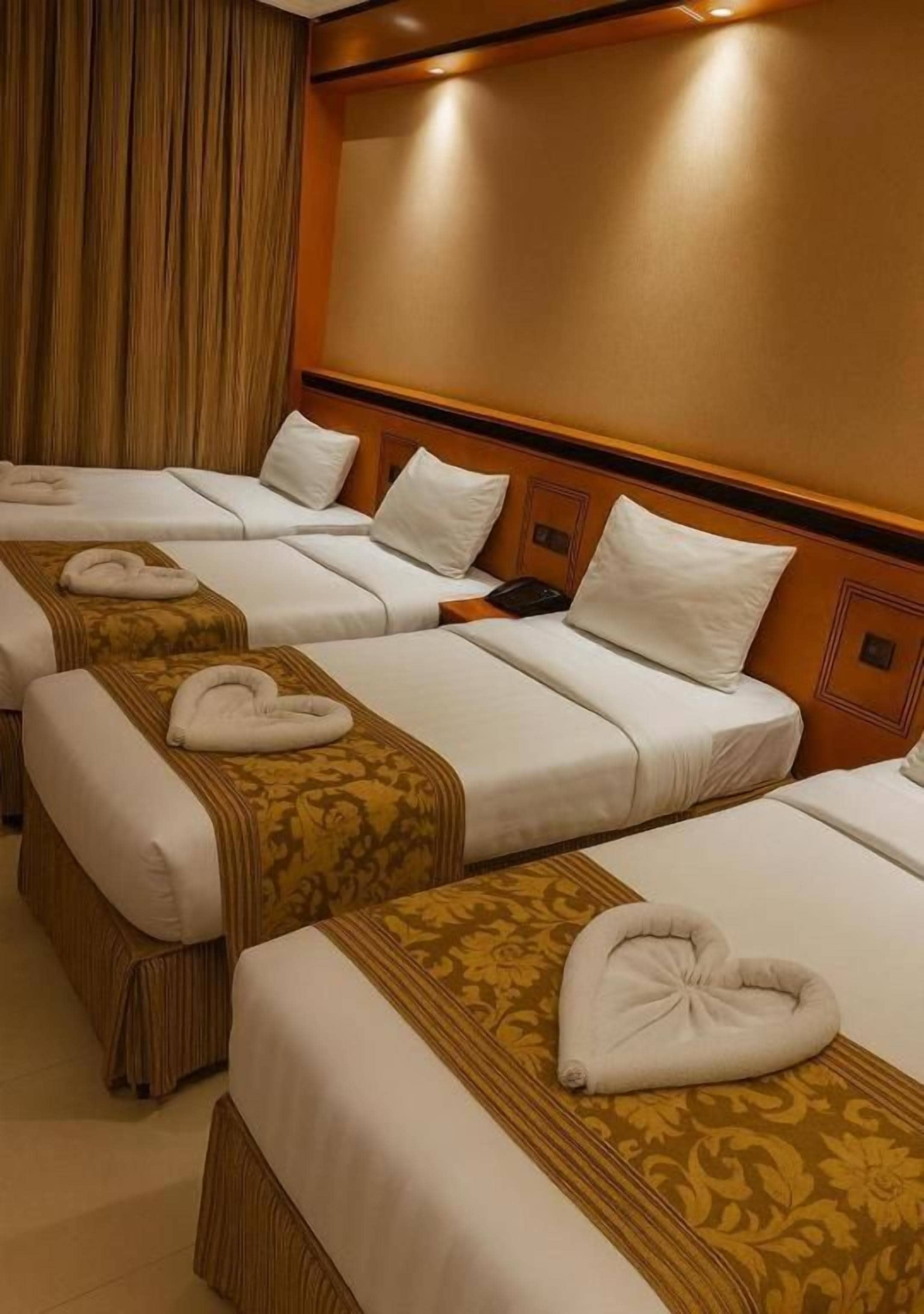 A hotel room with four beds arranged in a row, each with a white bedspread and a decorative headboard.