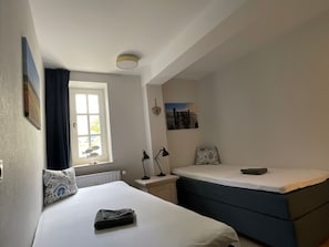 A bedroom with a bed, a bedside table with a lamp, a window with curtains, and a wall-mounted picture. - Villa Friedericia - Apt. 1 (Wyk auf Foehr)