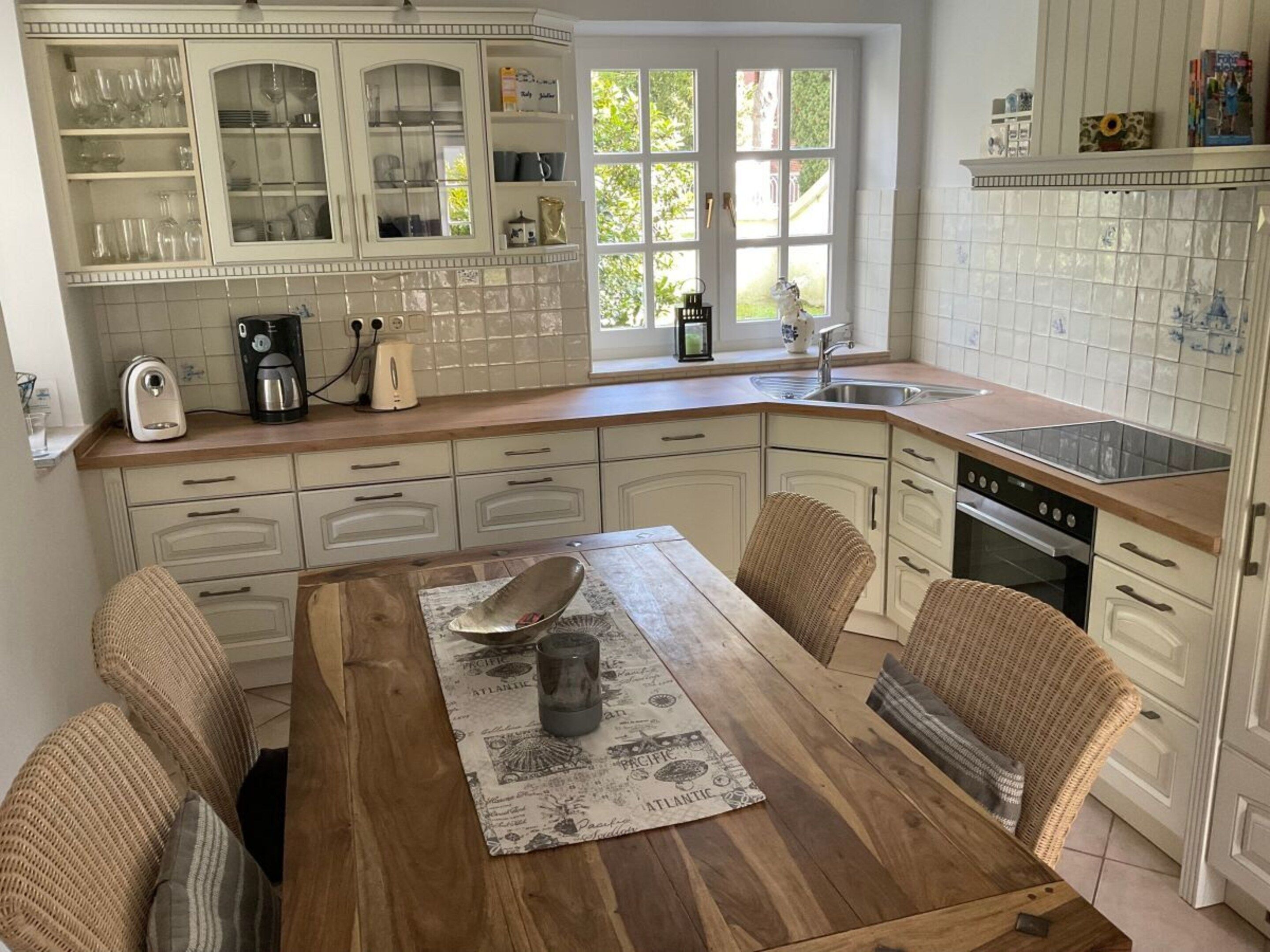 A kitchen with white cabinetry, a wooden dining table, wicker chairs, and a view of the outdoors through a window.