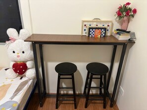 Eine kleine Küchenzeile mit einer Holzausstattung, zwei schwarzen Hocker, einem Teddybären, einem Radio und einer Vase mit Blumen.