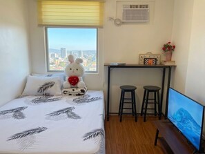 Ein Schlafzimmer mit einem Bett, einem Fenster mit Blick auf die Stadt, einem Schreibtisch mit zwei Hocker und einem Fernseher.