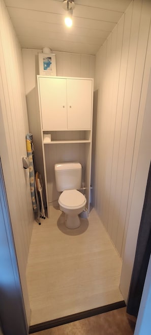 Un bagno stretto con il water, un armadietto sopra e uno spazio doccia a sinistra.