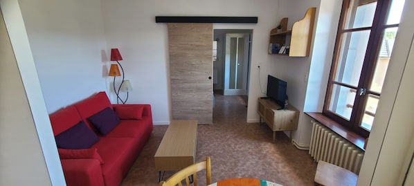Un soggiorno con un divano rosso, un piccolo tavolino, un mobile porta TV e un termosifone.