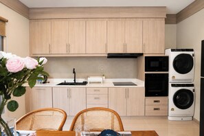 A modern kitchen with wooden cabinets, a black range hood, a built-in oven, and a stacked washer and dryer. - Tropical Escape New 2BR Villa with Private Pool (Tambon Rawai)