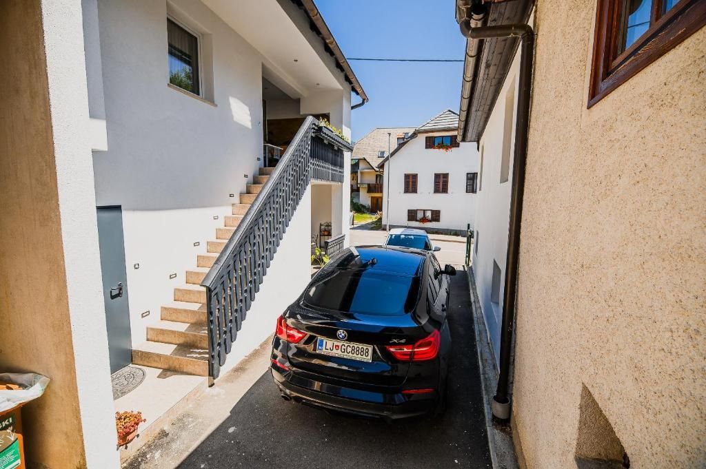 A narrow street with a black car parked on the side, a staircase leading to a building, and another building in the background.