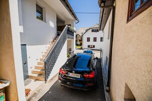 Una calle estrecha con un coche negro estacionado al lado, una escalera que lleva a un edificio y otro edificio al fondo.