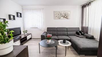 A modern living room with a sectional sofa, a flat-screen TV, a coffee table, and a potted plant.