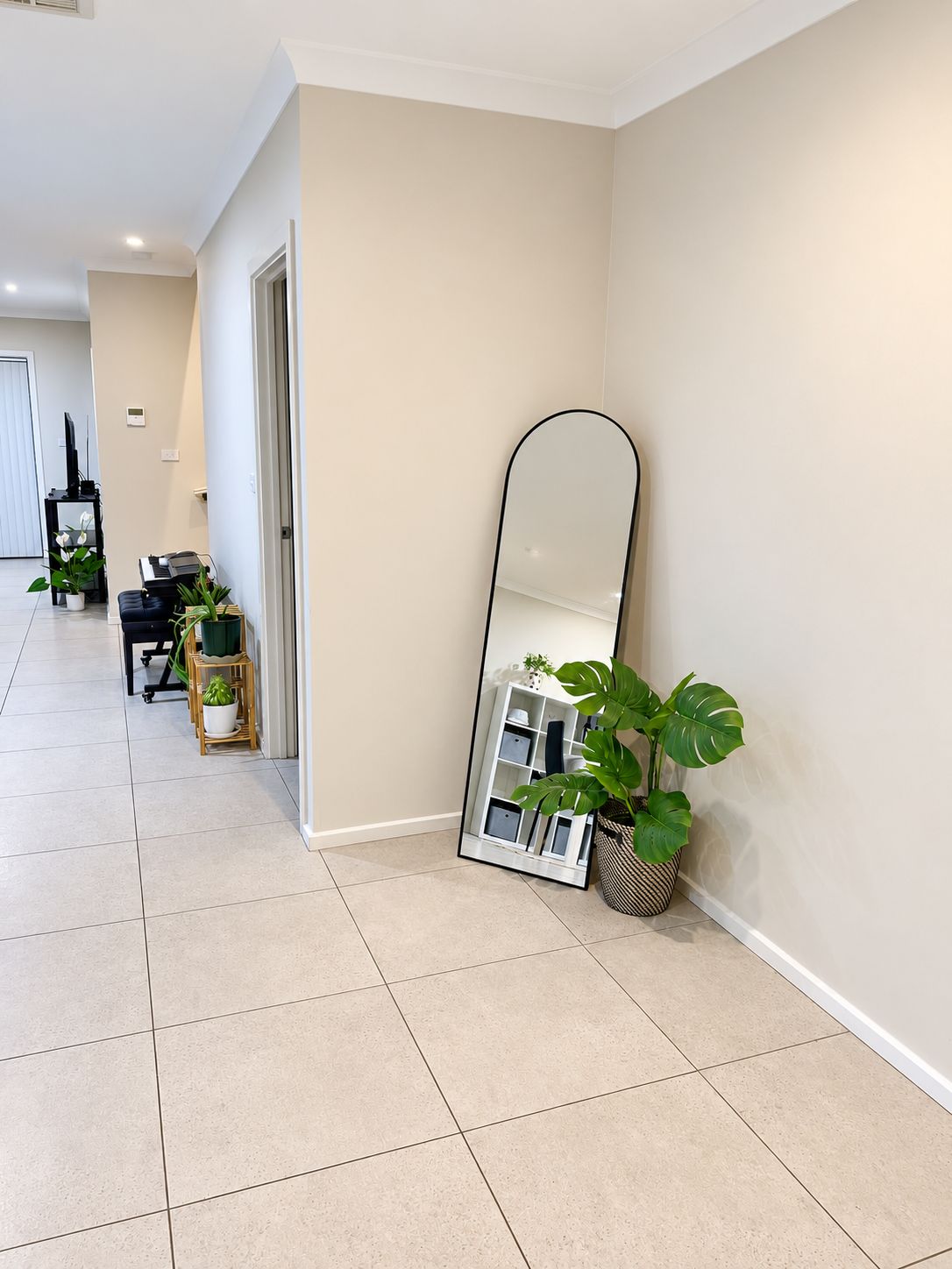 A hallway with a tiled floor, a large mirror leaning against the wall, and potted plants.