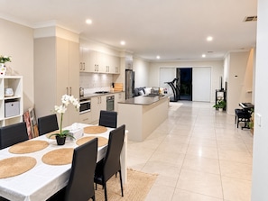 A modern kitchen with white cabinets, a central island, and a dining area with a table set for four. - Stylish 4-Bed Terrace | Modern & Convenient (Throsby)