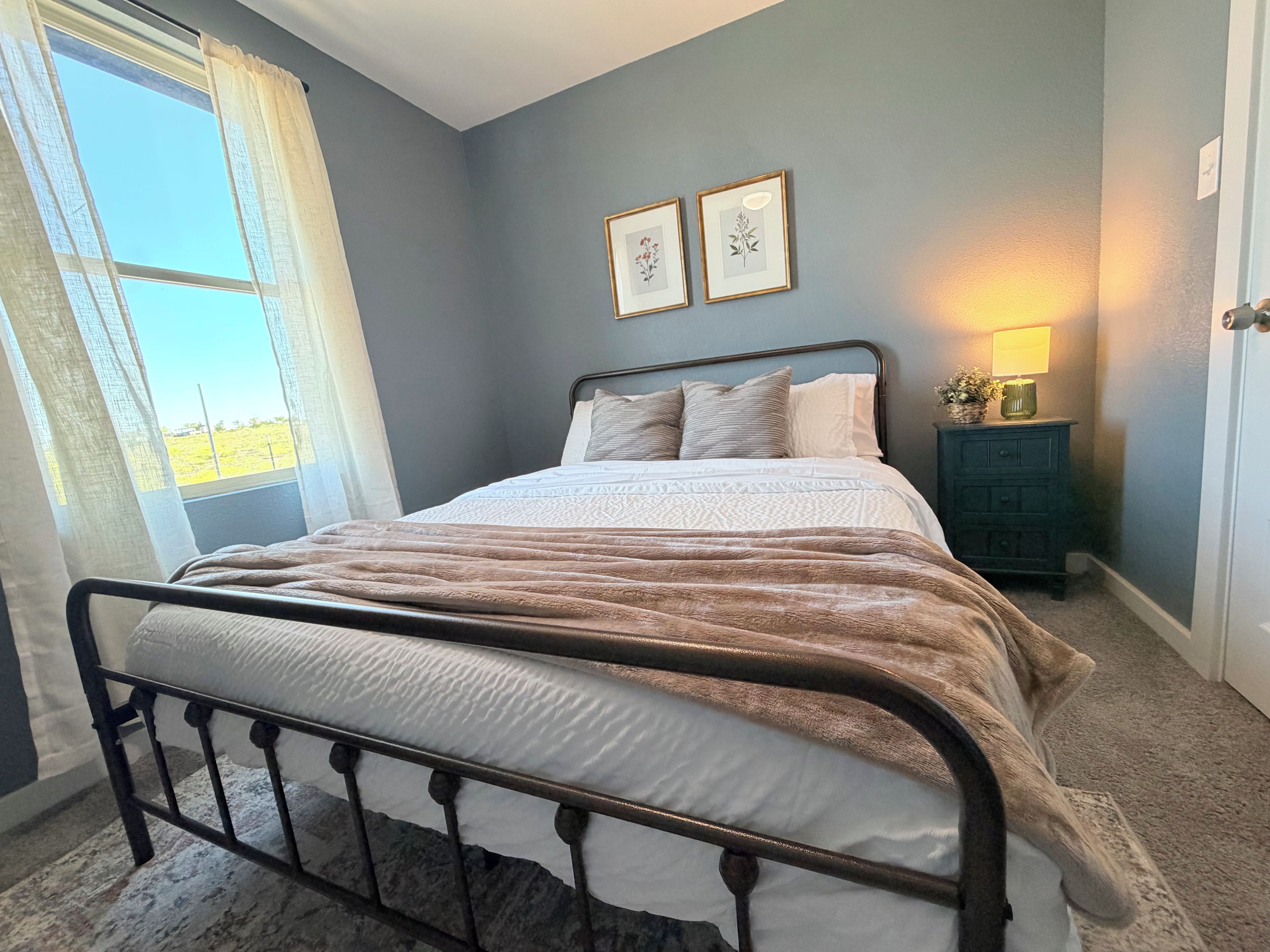A bedroom with a bed, a nightstand, a lamp, and a window with curtains.
