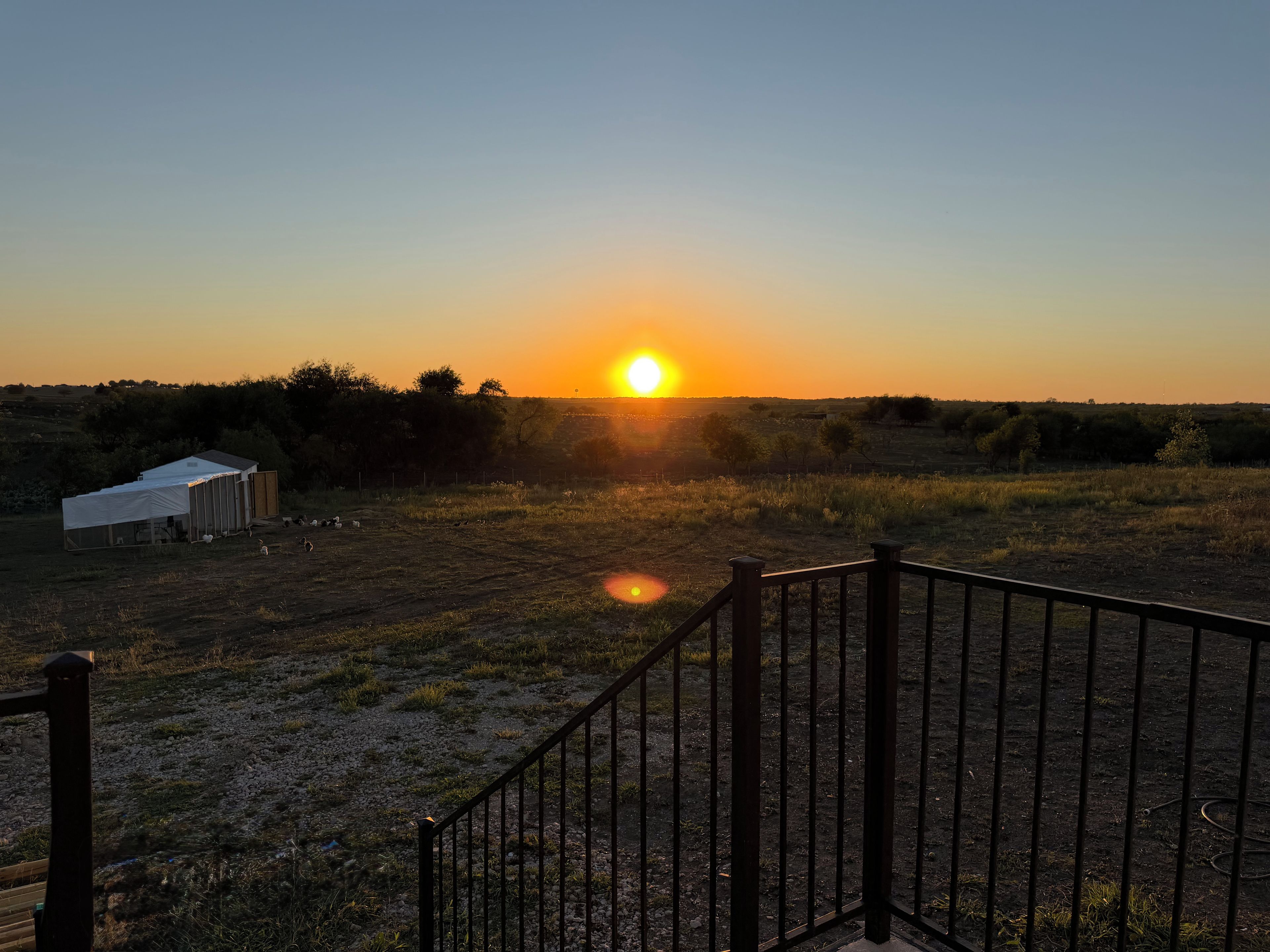 Ein Sonnenuntergang über einem Feld mit einem eingezäunten Bereich und einer kleinen Struktur.