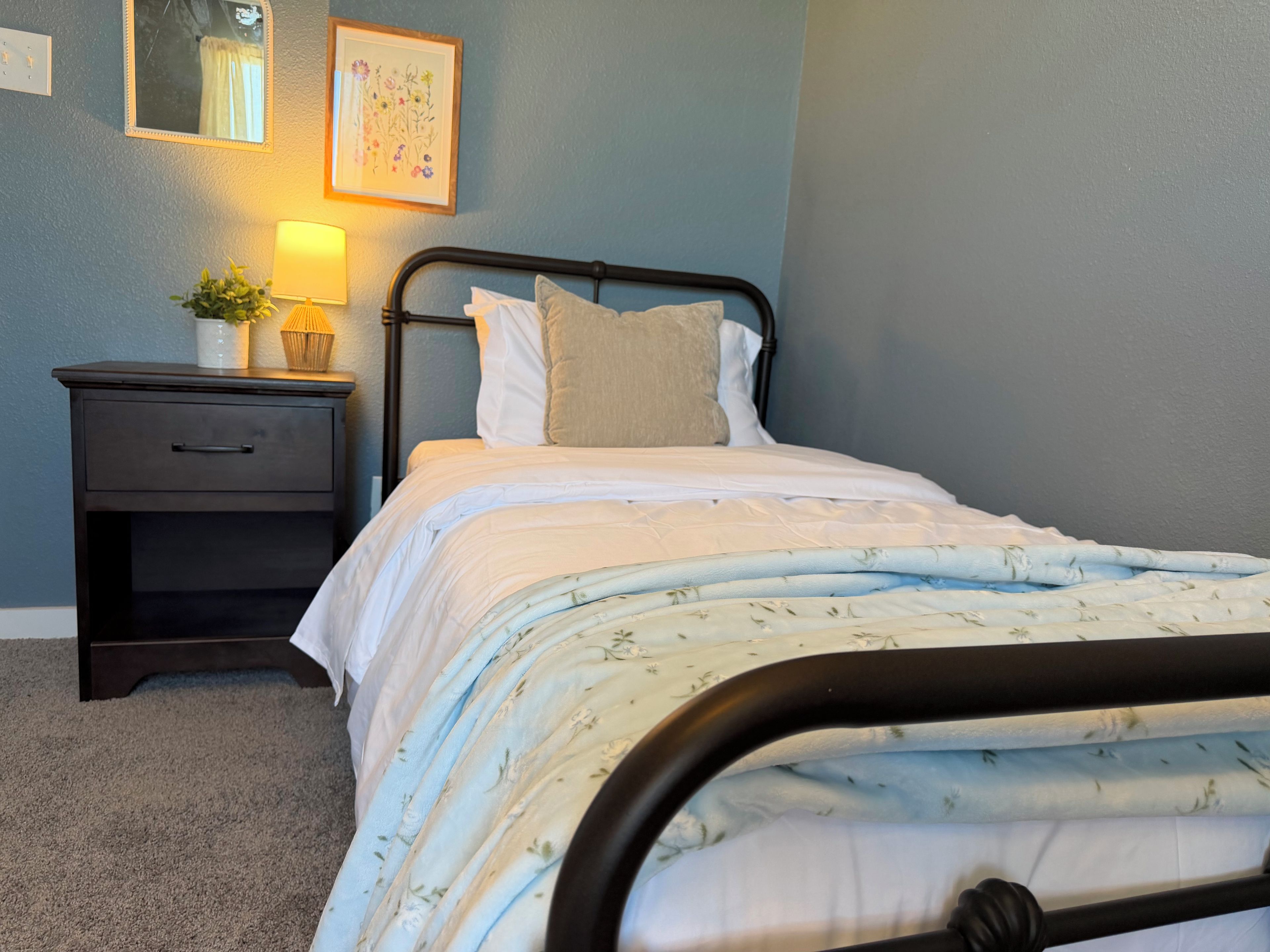 A bedroom with a bed, a nightstand, a lamp, and a framed floral artwork on the wall.