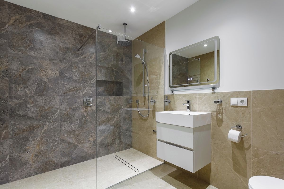 Un baño moderno con ducha envuelta en vidrio, un lavabo blanco y un espejo encima.