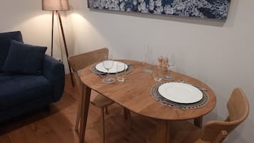 Et spiseområde med et træbord dækket til to personer, to stole, en blå sofa og en gulvlampe.