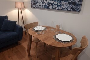 Et spiseområde med et træbord dækket til to personer, to stole, en blå sofa og en gulvlampe.