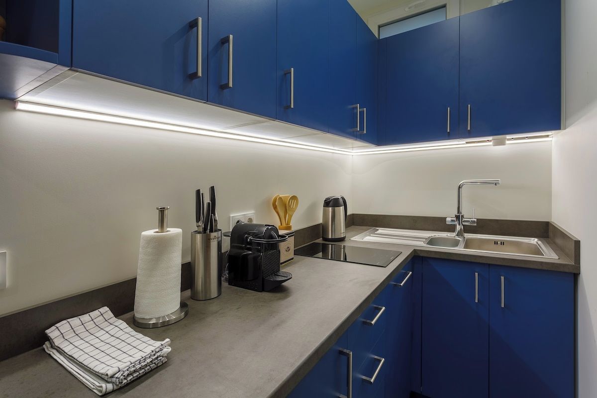 A modern kitchen with blue cabinets, stainless steel appliances, and a countertop with various utensils and a paper towel holder.