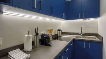 A modern kitchen with blue cabinets, stainless steel appliances, and a countertop with various utensils and a paper towel holder.