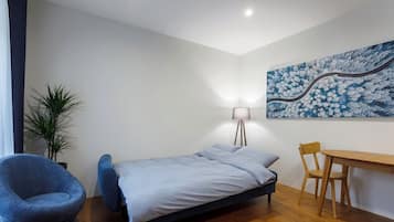 A bedroom with a bed, a desk, a chair, a lamp, and a wall painting.
