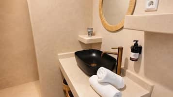 Une salle de bain moderne avec une douche à forme incurvée, un miroir rond, un lavabo noir et un porte-serviettes.