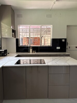 A modern kitchen with a large island, built-in appliances, and a window with decorative bars. - Hillside Home Bulawayo (Bulawayo)