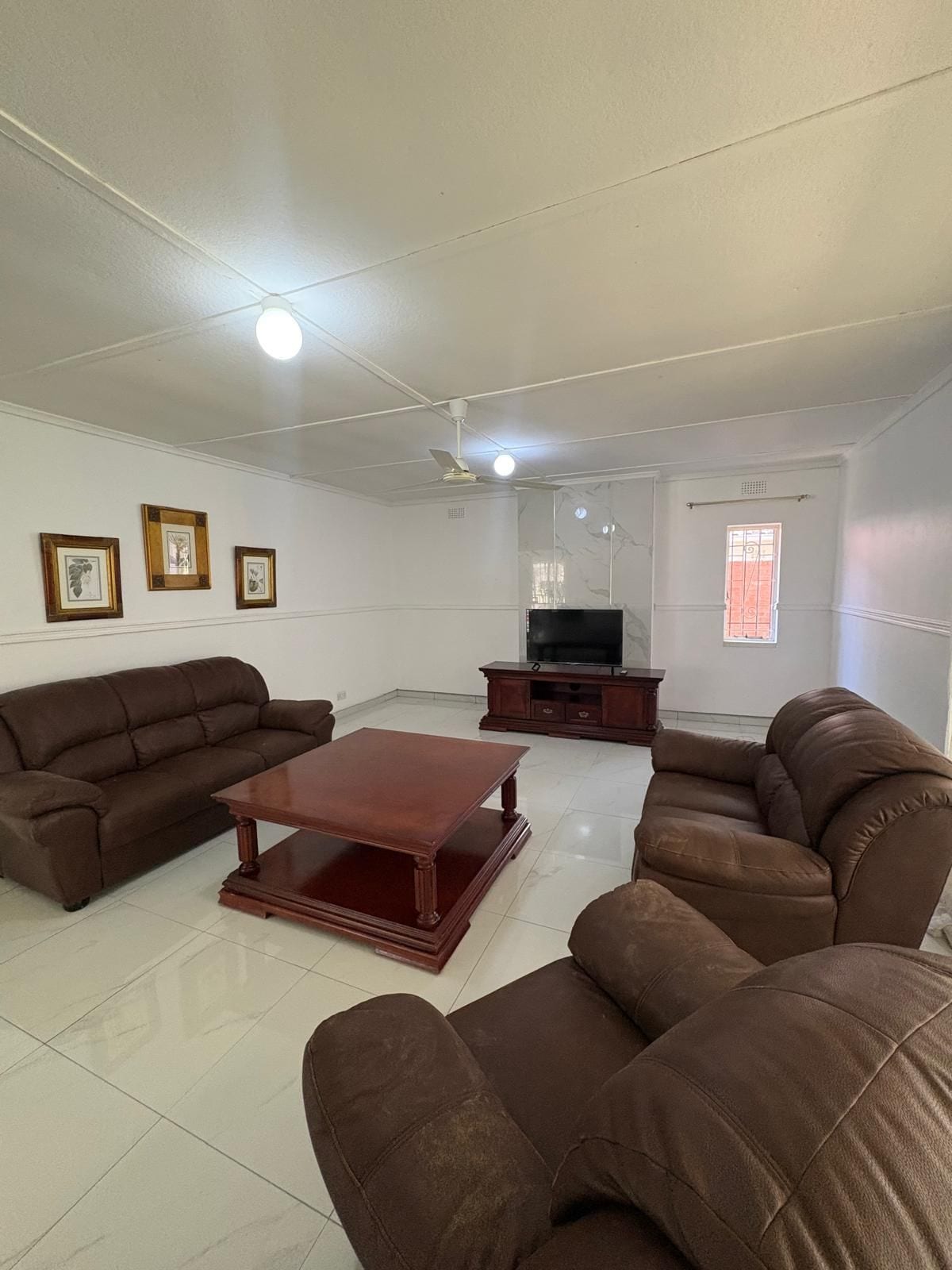 A living room with a brown sofa set, a wooden coffee table, a TV stand, and framed pictures on the wall.