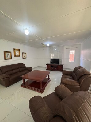 A living room with a brown sofa set, a wooden coffee table, a TV stand, and framed pictures on the wall. - Hillside Home Bulawayo (Bulawayo)