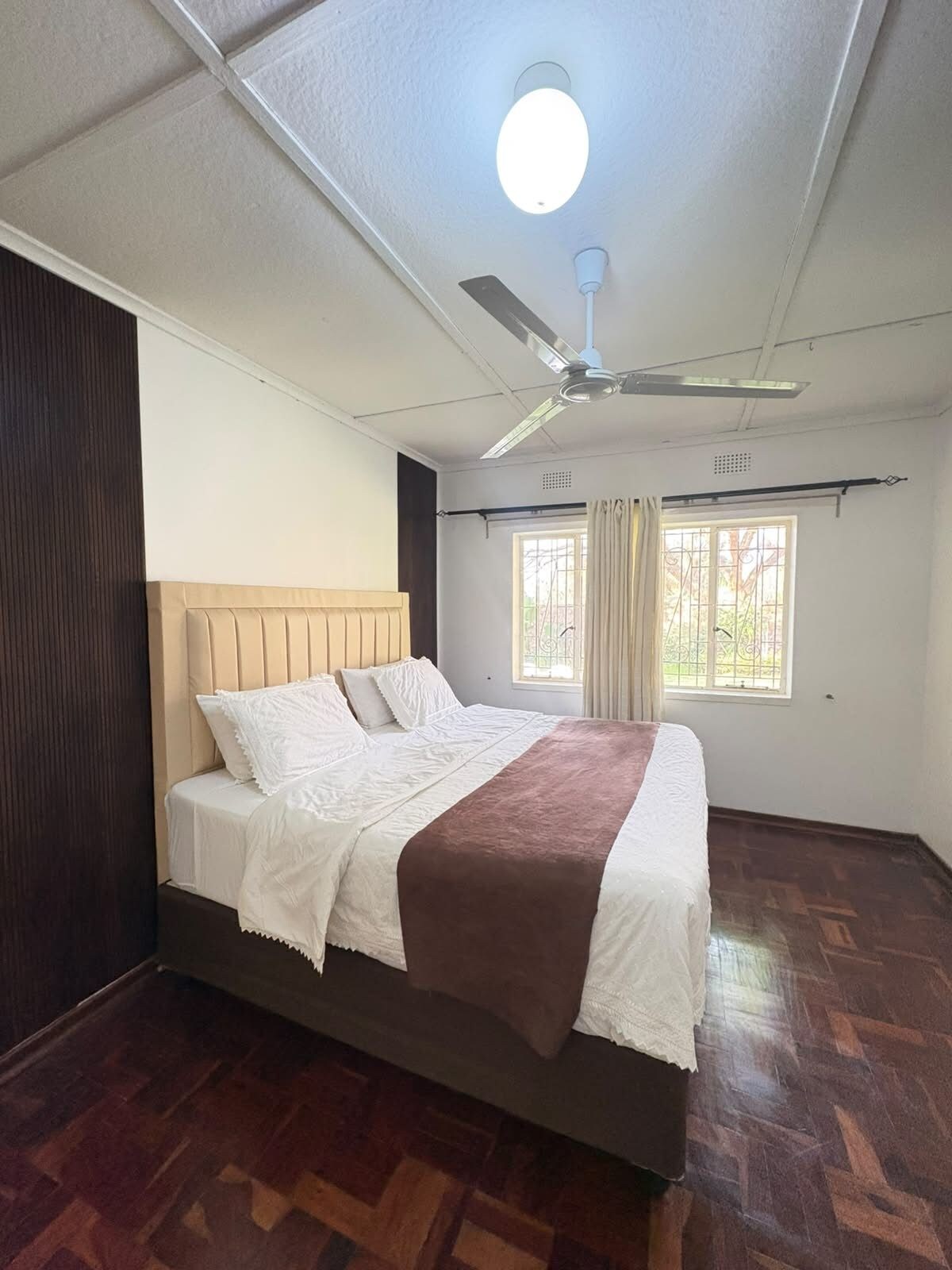 Une chambre à coucher avec un lit, un ventilateur de plafond et une fenêtre avec des rideaux.