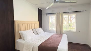 Une chambre à coucher avec un lit, un ventilateur de plafond et une fenêtre avec des rideaux.