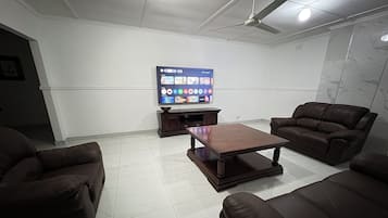 Ett vardagsrum med en platt-TV, mörkbruna lädersoffor, ett soffbord i trä och en takfläkt.