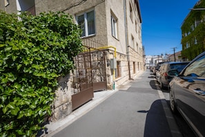 Eine schmale Straße mit geparkten Autos, einem Metallgitter und einem Gebäude mit Steinmauern.