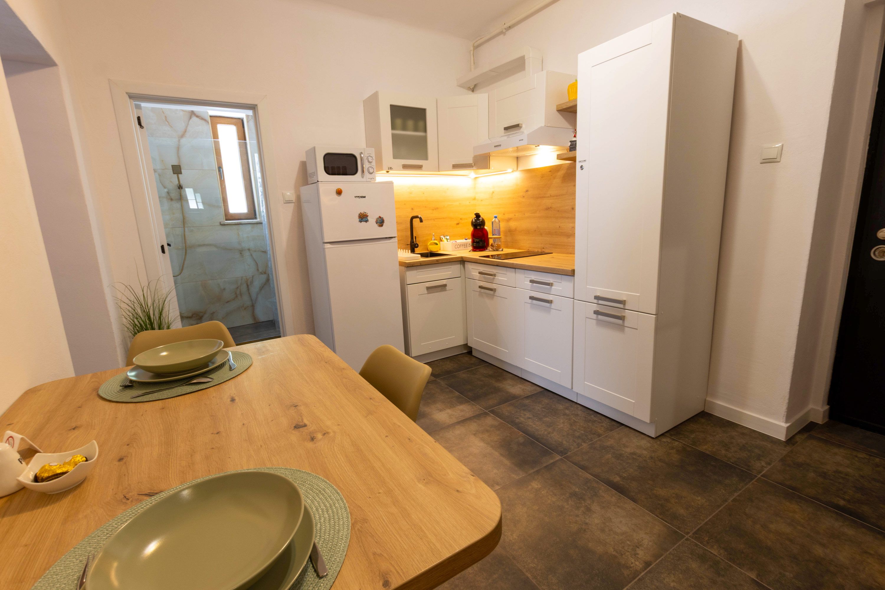 A compact kitchen with white cabinets, a built-in oven, and a sink. There's a dining table with a green placemat and a bowl.
