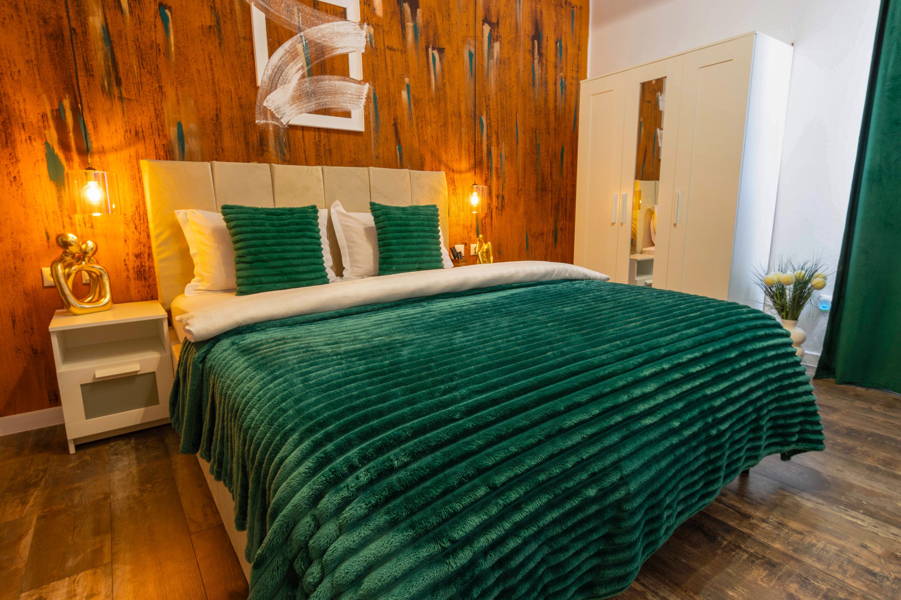 A bedroom with a wooden headboard, a green bedspread, bedside tables with lamps, and a wardrobe.