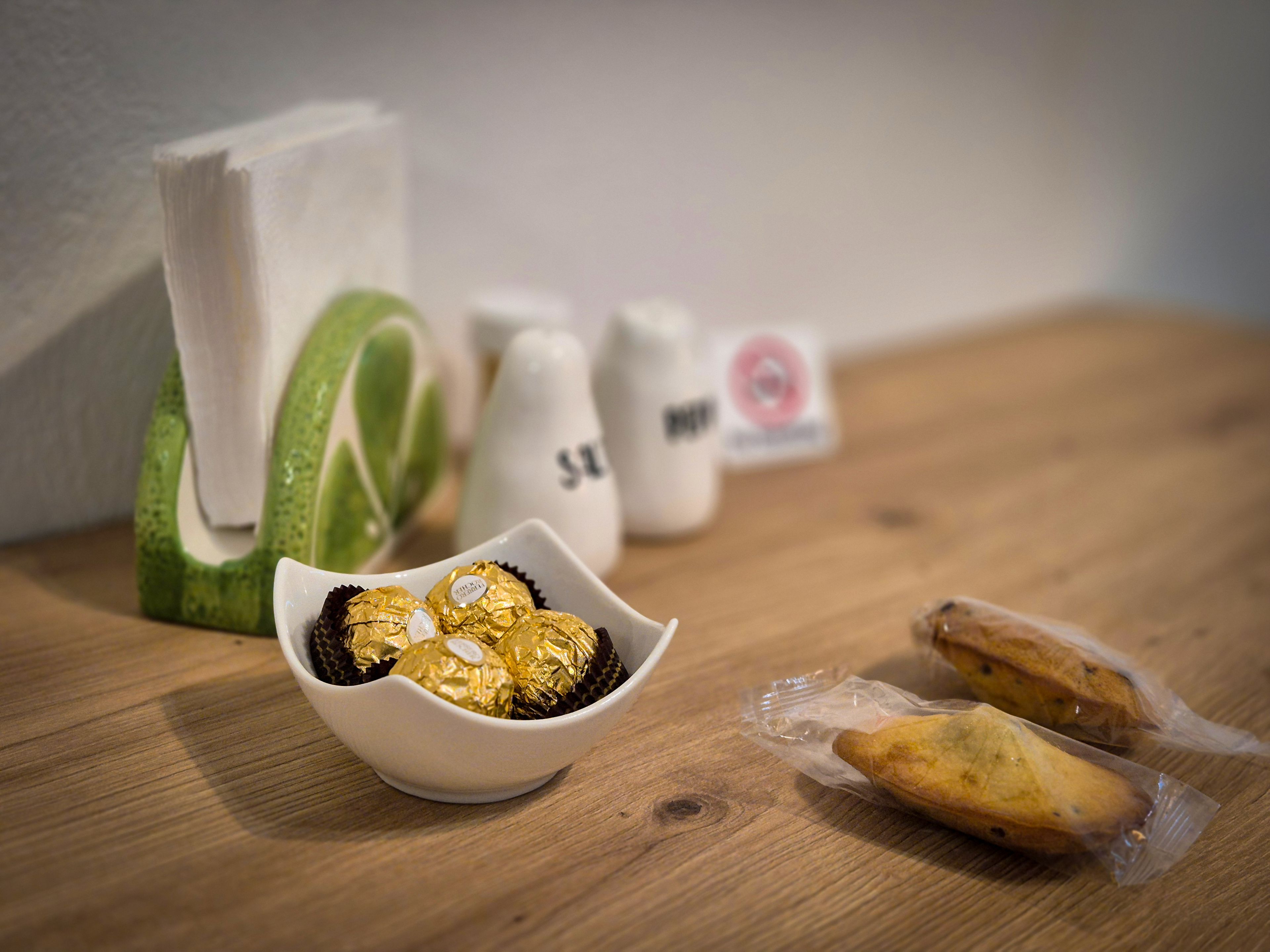 A wooden table with a bowl of wrapped chocolates, a green and white object, and two small packages.