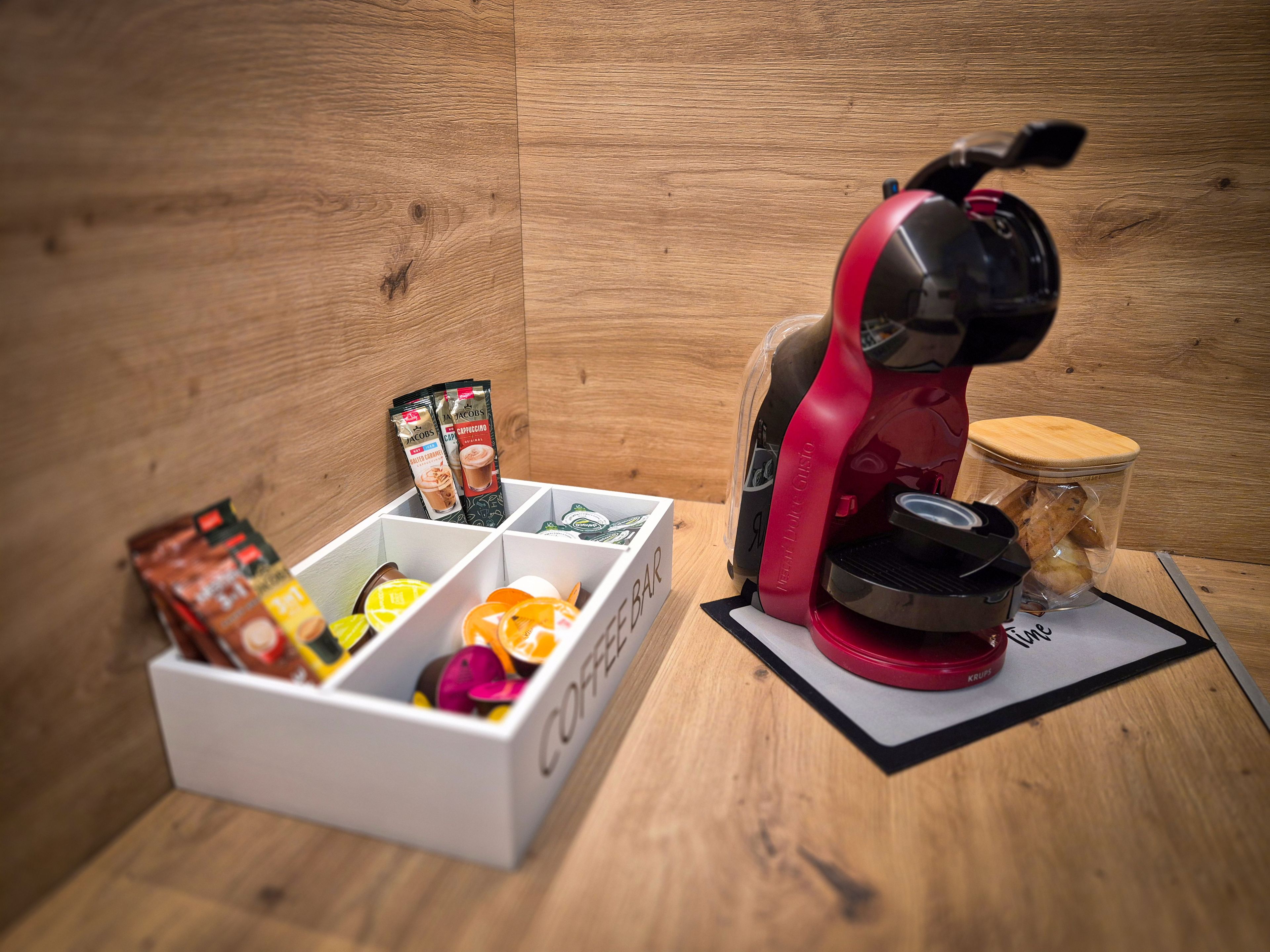Une machine à café, une boîte de capsules de café et un bocal de biscuits sur une surface en bois.