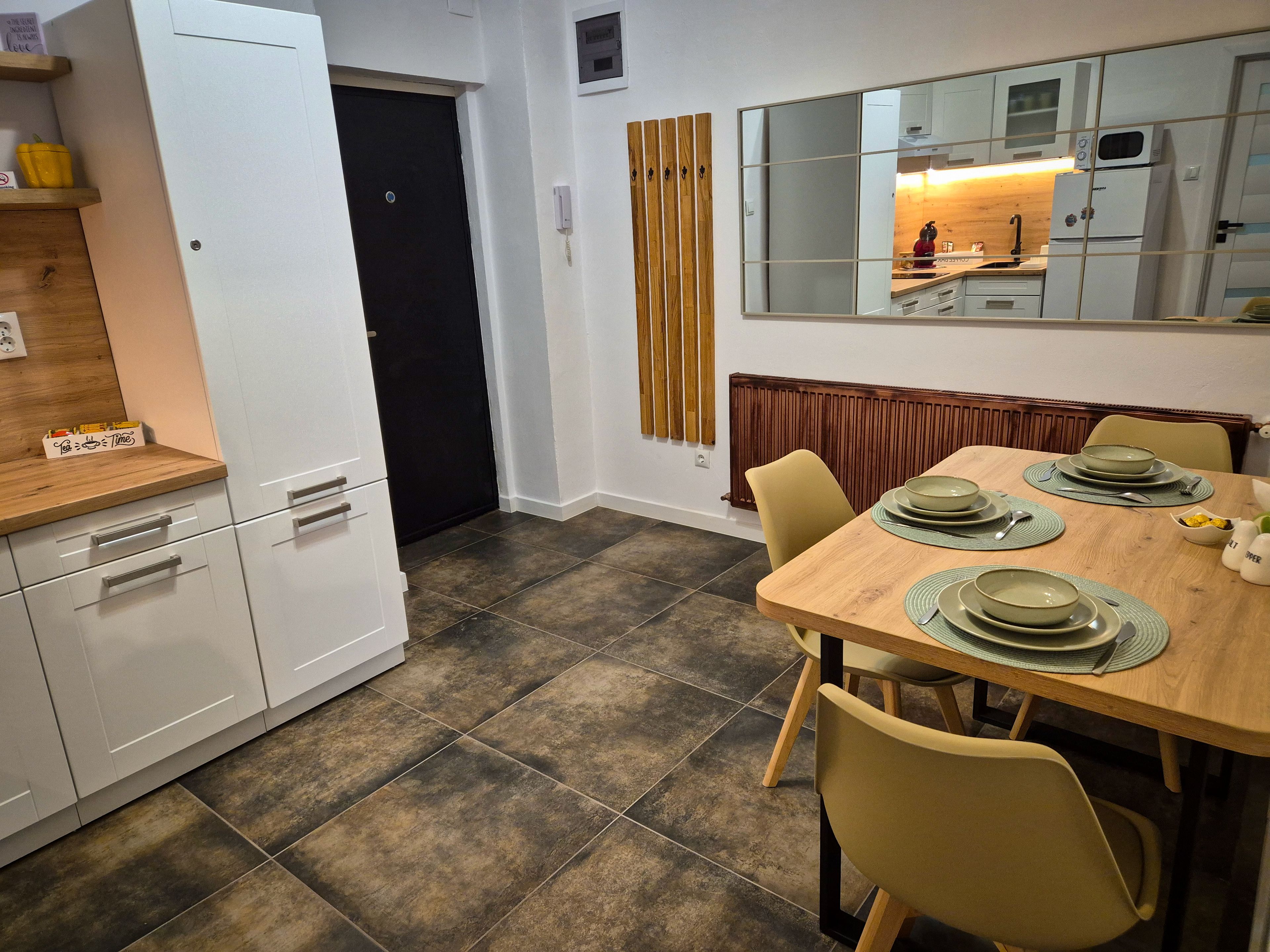 Una cocina moderna con armarios blancos, una encimera de madera, una mesa de comedor preparada con platos y tazones, y un espejo grande sobre la mesa.