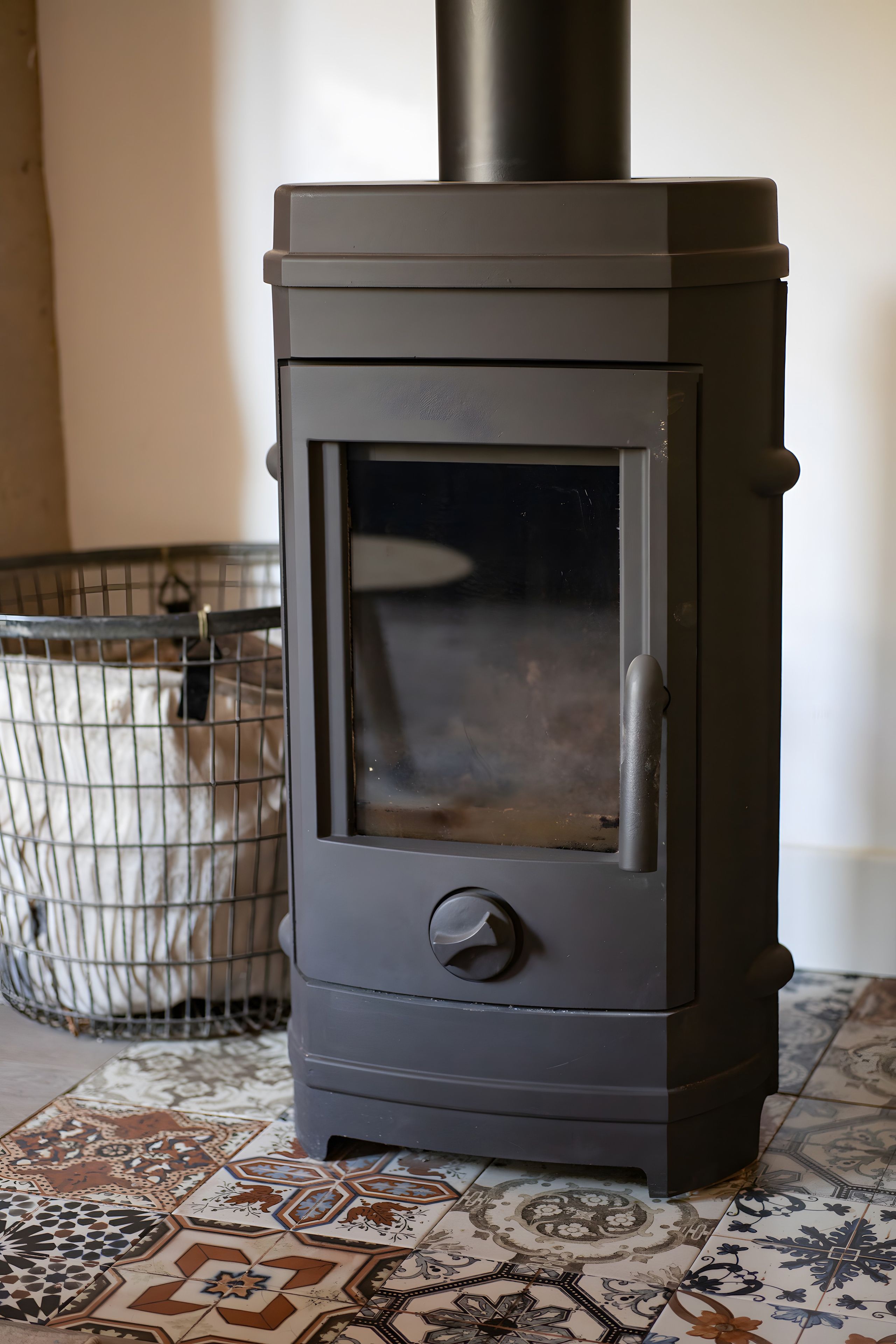 Un poêle à bois noir avec une porte en verre, une cage en métal et des carreaux de sol à motifs.