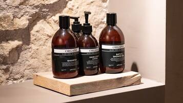 Tre flaconi di shampoo, lozione e gel doccia biologici su uno scaffale di legno, con una parete strutturata sullo sfondo.