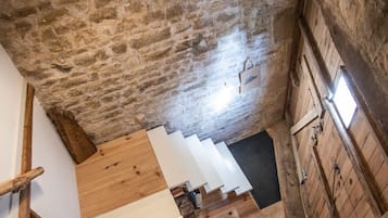 Eine Treppe mit hölzernen Stufen führt zu einer unteren Ebene, eine Steinmauer und eine abgehängte Leuchte.