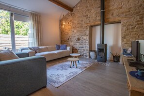 A cozy living room with a stone wall, a sofa, a small table, and a wood-burning stove.