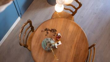 Une table de salle à manger ronde en bois, avec des chaises, un vase contenant des fleurs séchées et une bouteille posée sur la table.