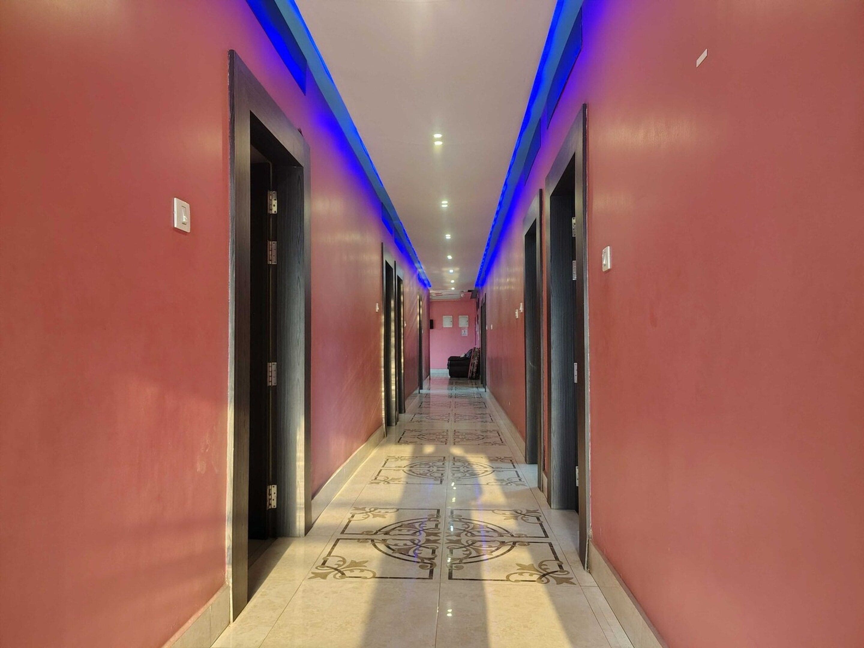 A hotel hallway with a patterned floor, doors on both sides, and blue lighting on the ceiling.