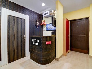 A hotel reception area with a reception desk, a clock, a television, and a closed door. - Deluxe PG Guest House (Barasat)