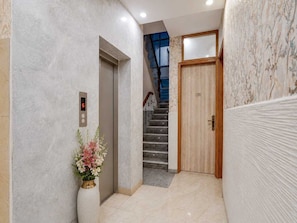 Un pasillo con pared de mármol, una puerta de madera con la etiqueta '201' y una escalera con barandilla azul.