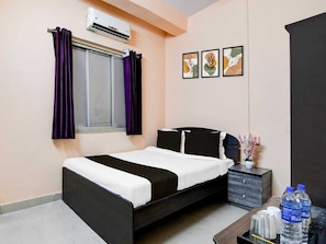 Habitación de hotel con cama, mesita de noche, cómoda, unidad de aire acondicionado y ventana con cortinas moradas.