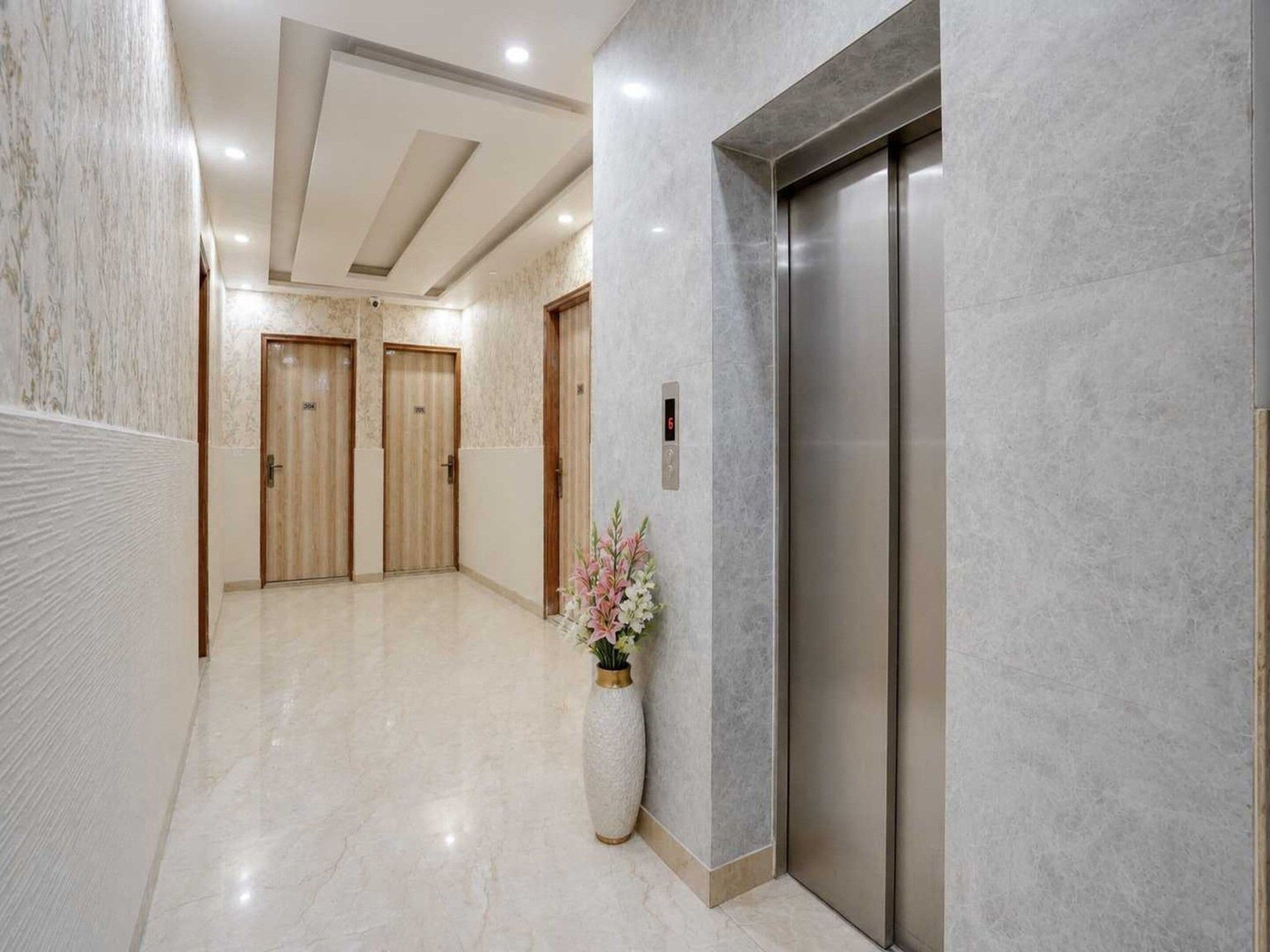 A hallway with a marble floor, wooden doors, and a large vase with flowers.